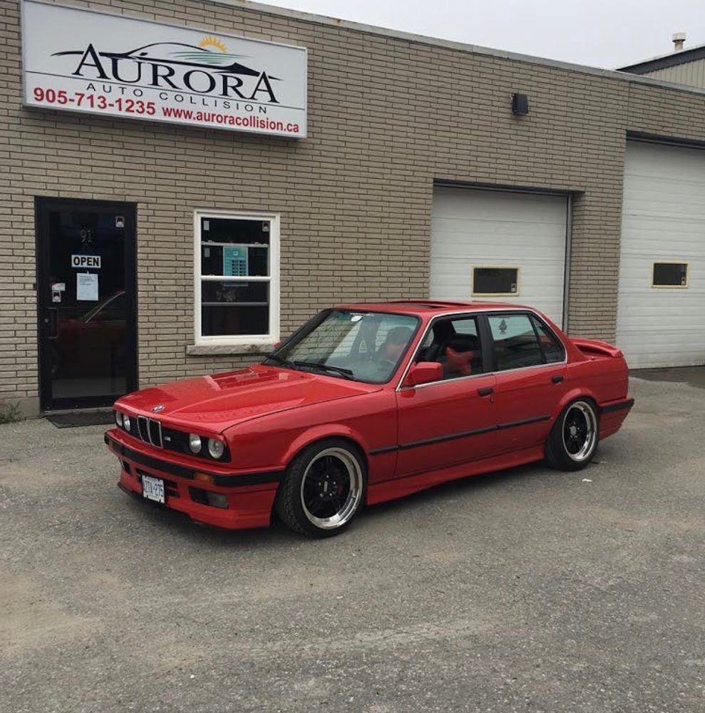 A red car standing outside the Aurora Auto Collision & Repairs Shop